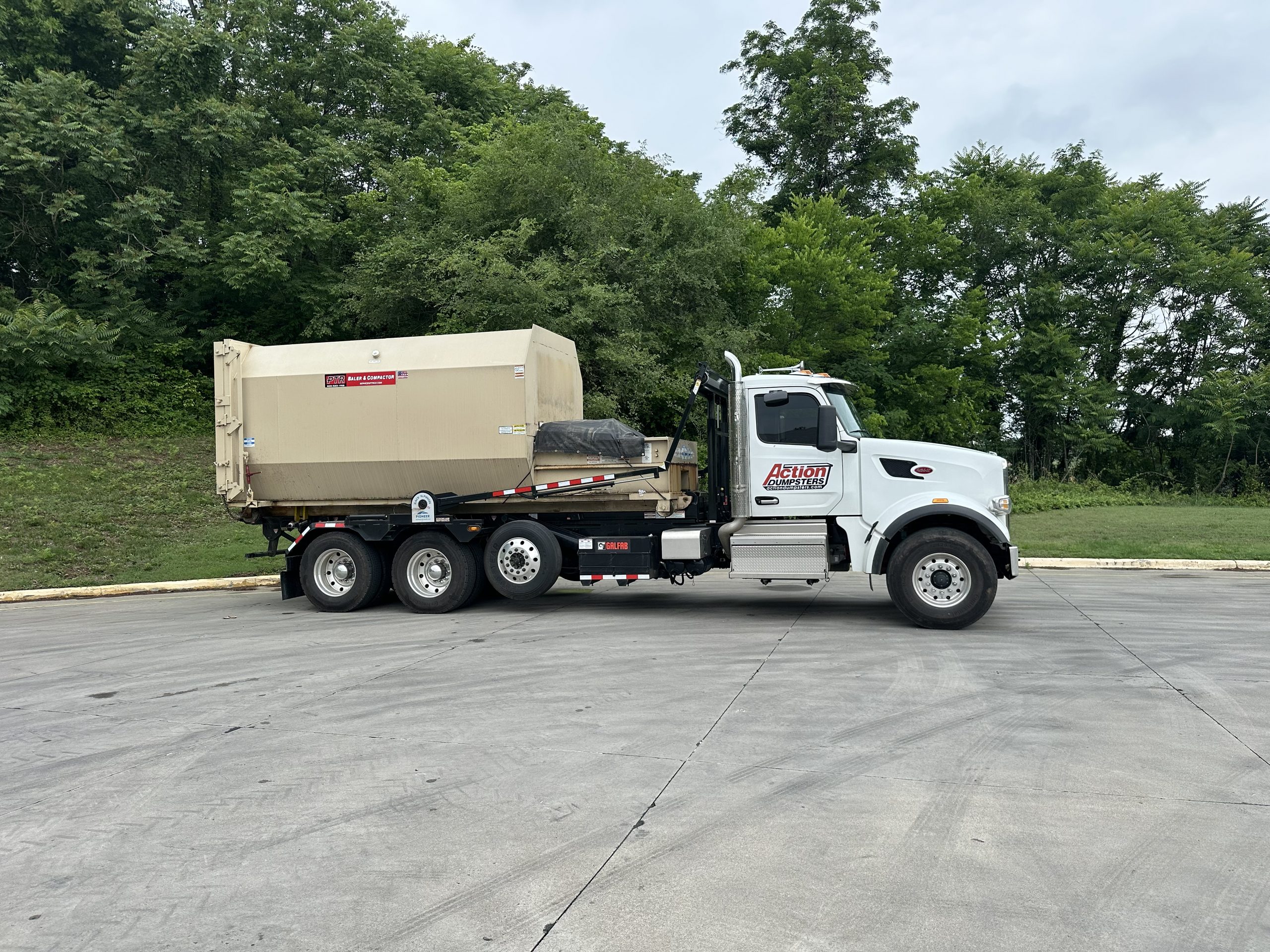 Action Dumpsters truck loaded with a commercial trash compactor