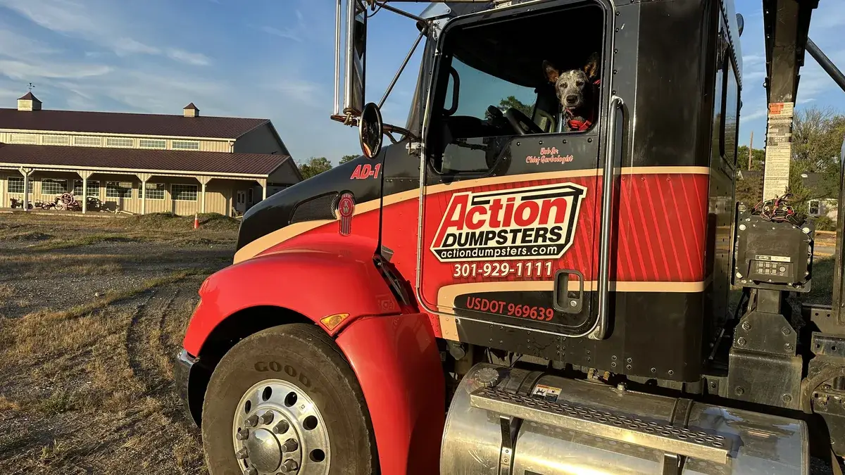Action Dumpsters truck cab with a dog in the window and a barn behind it, serving Brookeville, MD