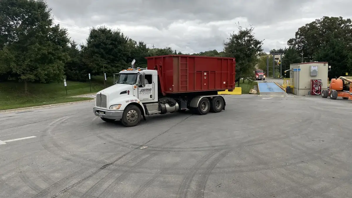 Action Dumpsters truck carrying a red roll-off container on a paved lot, Clarksburg, MD