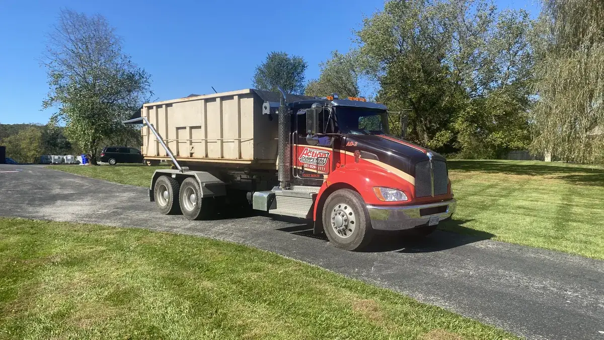 Action Dumpsters truck delivering a tan roll-off dumpster on a paved drive beside a lawn, serving Clarksville, MD