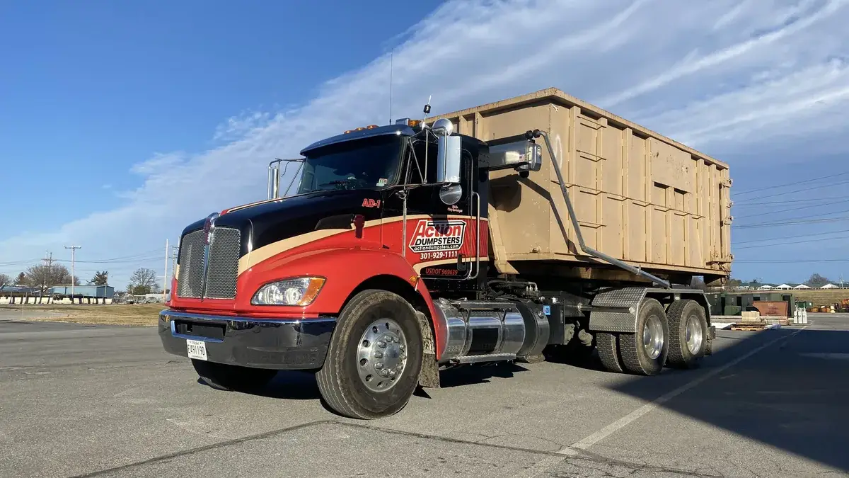 Red and black Action Dumpsters roll-off truck carrying a tan dumpster on an airfield ramp in Frederick, MD