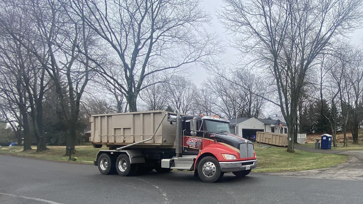 Action Dumpsters roll-off truck with a tan dumpster on a residential street in Germantown, MD