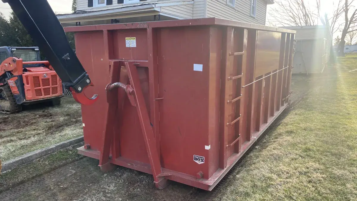 Red roll-off dumpster beside a house with an excavator behind it at a Mount Airy, MD job