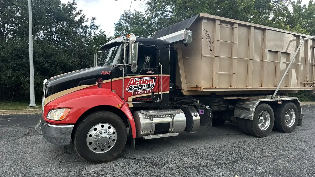 Red and black Action Dumpsters roll-off truck carrying a tan dumpster in Montgomery County, MD