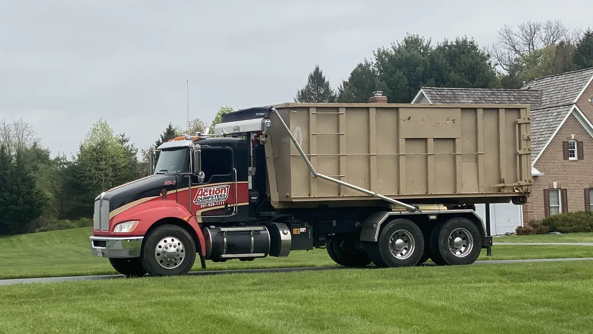Red and black Action Dumpsters truck carrying a tan roll-off dumpster in Redland, MD