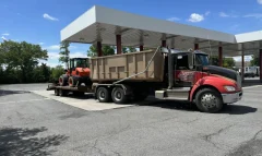Action Dumpsters truck with a 20 yard dumpster, towing an orange wheel loader on a trailer