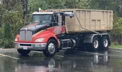Action Dumpsters roll-off truck carrying a 25 yard dumpster in a wet parking lot